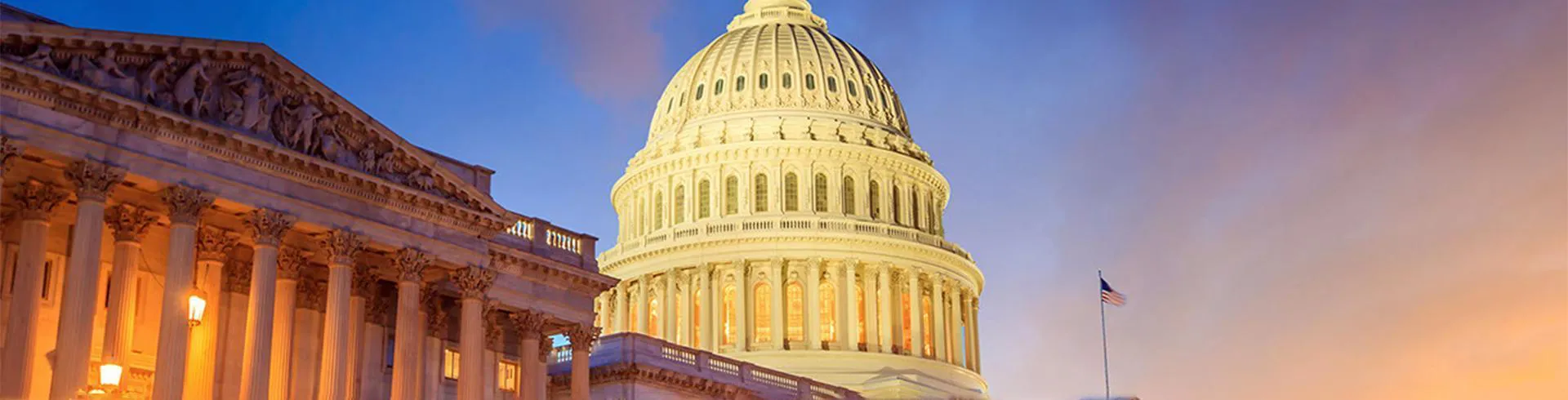 Western facade of the United States Capital building dramatically lit with street and flood lights in front of the darkening sky from a setting sun behind the camera