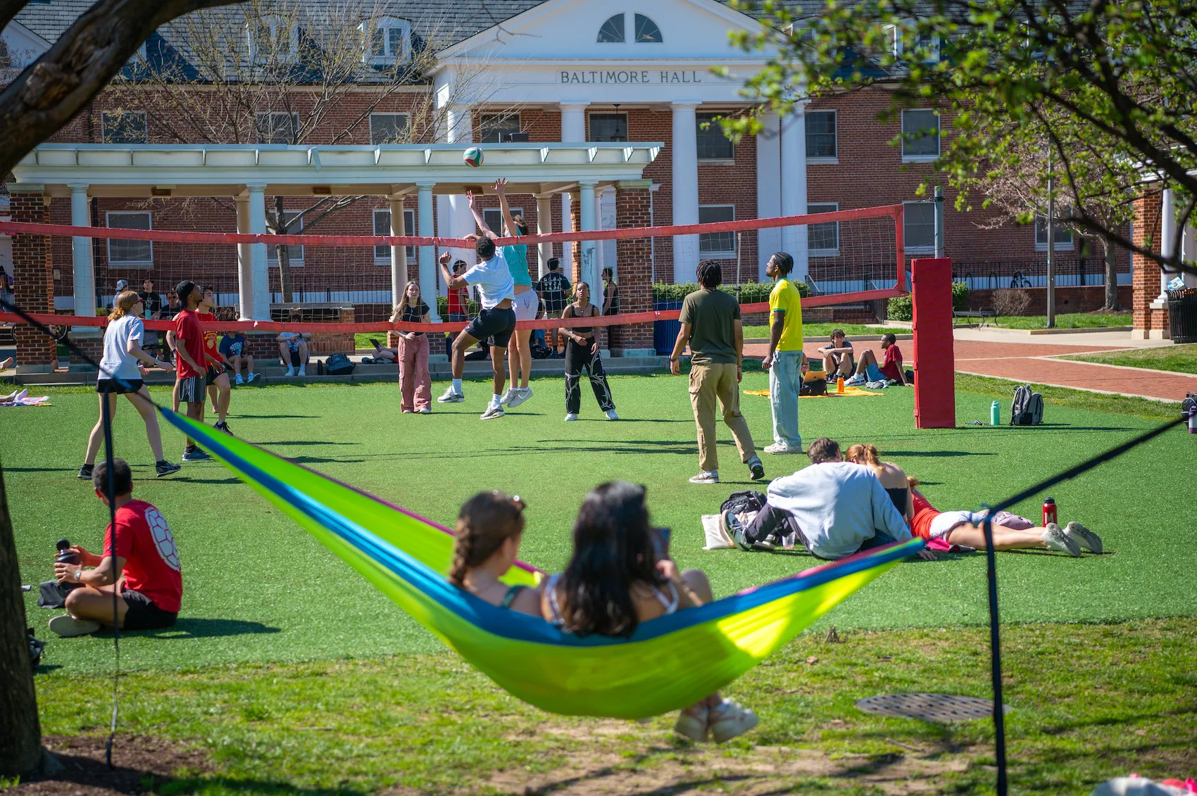 Students picnic, play volleyball, and swing in a hammock in front of Baltimore Hall