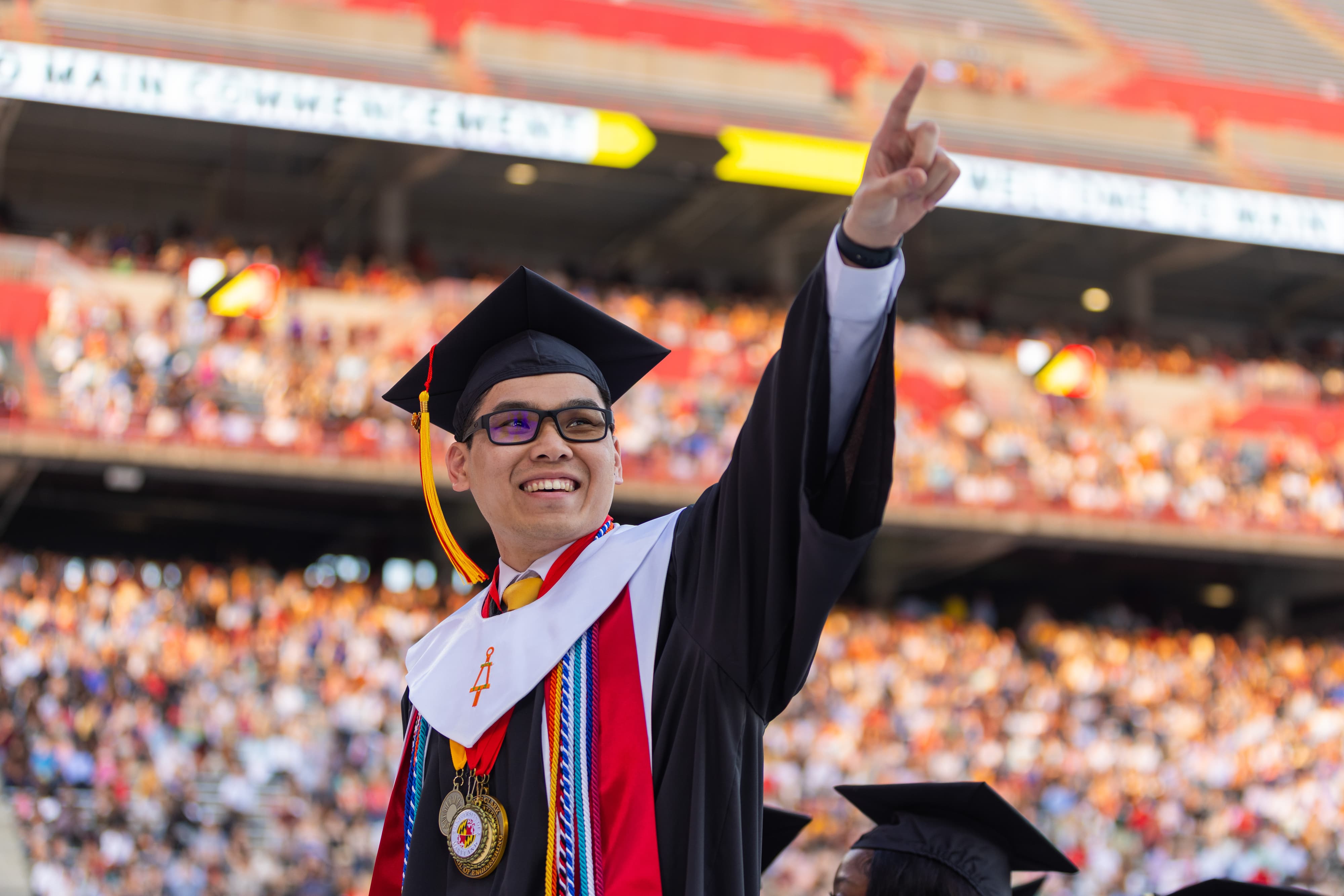 A graduate pointing towards a crowd in the stadium