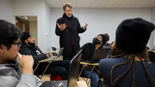 A man stands as he teaches a room of students seated at desks